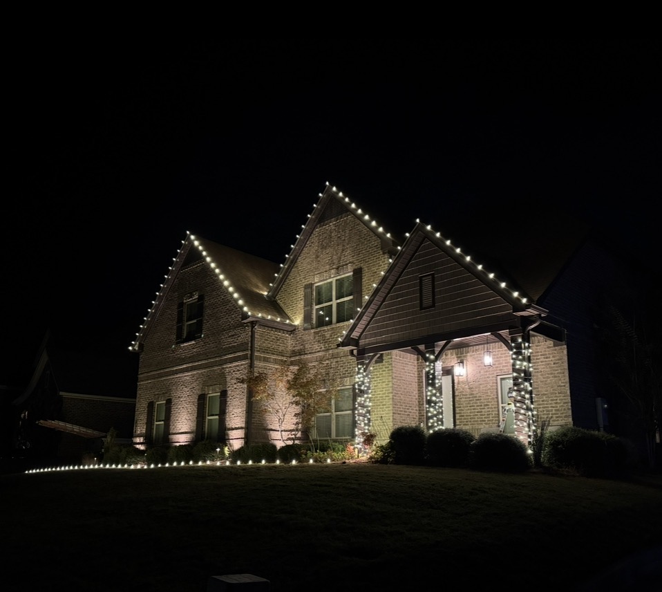 Brick home with dramatic peaked rooflines outlined in lights